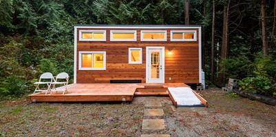 Tiny House in der Dämmerung vor einem Wald.