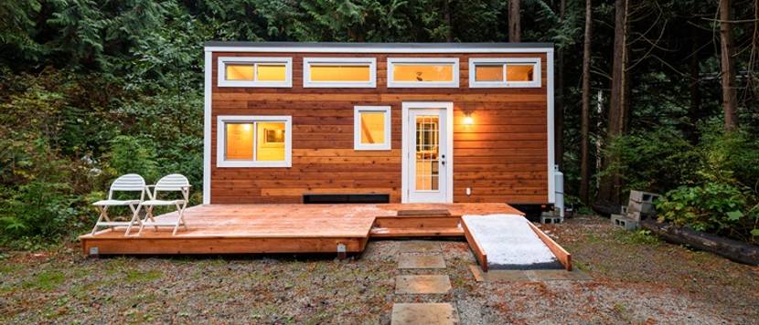 Tiny House in der Dämmerung vor einem Wald.