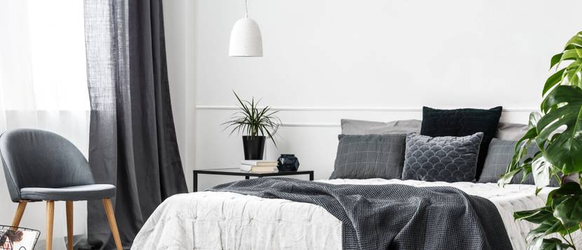 Grau-weiß eingerichtetes Schlafzimmer mit Bett, Stuhl und Gardinen.