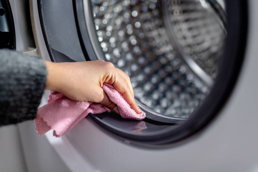 Hand reinigt die Türdichtung einer Waschmaschine mit einem Tuch.