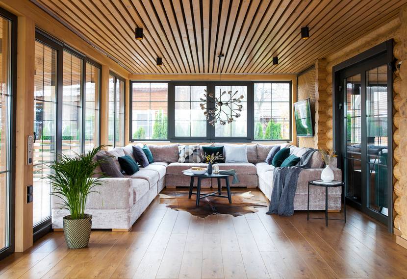 In einem Wintergarten mit hölzerner Decke und Wänden steht ein großes Sofa.