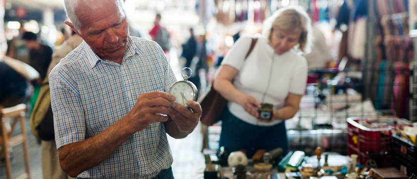 älterer mann schaut sich uhr auf einem flohmarkt an