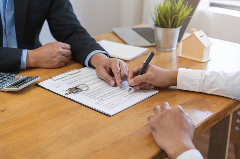 Ein Vertrag wird unterschrieben, daneben liegen Schlüssel auf dem Tisch.