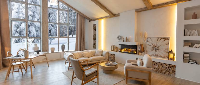 Wohnzimmer eines Hauses im Landhausstil mit großen Fenstern und Blick auf winterlichen Wald.