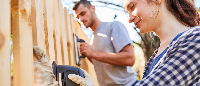 Frau und Mann bauen einen Gartenzaun aus Holz.